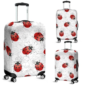May include: A white luggage cover with a black and white floral pattern and red ladybugs. The luggage cover is shown on a suitcase.