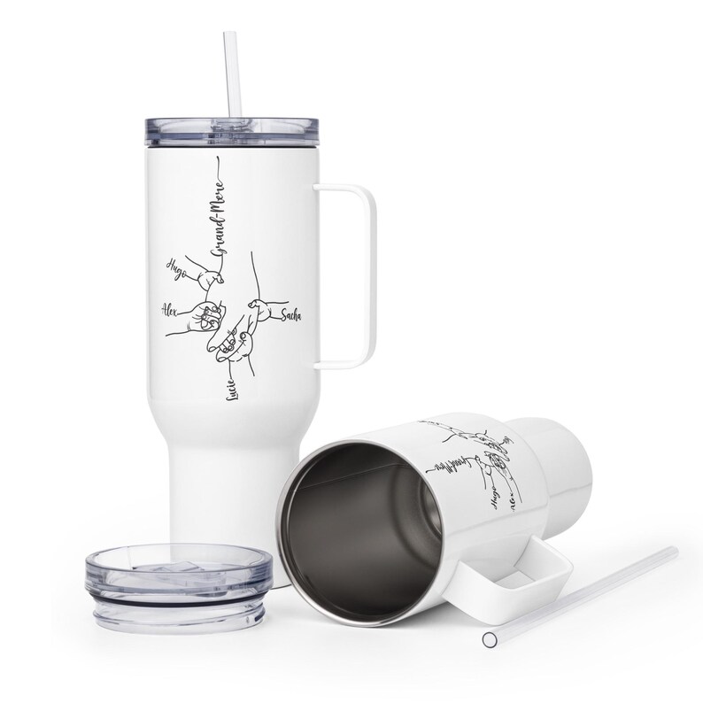 May include: White insulated tumbler with a handle, straw, and lid. The tumbler features a black line drawing of hands and the word "Grand-Mere" with names. One tumbler is upright, and another is on its side.