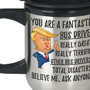 Könnte beinhalten: Eine silberne Reise-Thermoskanne mit schwarzem Deckel und Griff. Die Tasse zeigt ein Cartoon-Bild eines Mannes mit blonden Haaren und einem blauen Anzug. Der Text auf der Tasse lautet: "You are a fantastic bus driver. Really great. Really terrific. Other bus drivers? Total disasters! Believe me. Ask anyone."