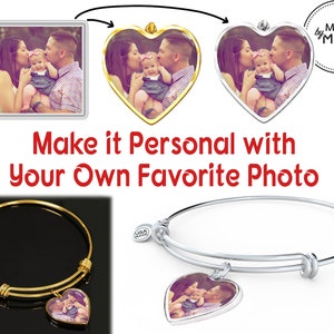 May include: A gold bangle bracelet with a heart-shaped charm that can be personalized with a photo. The charm features a family of three, a mother, father, and child. The bracelet is made by Moms.
