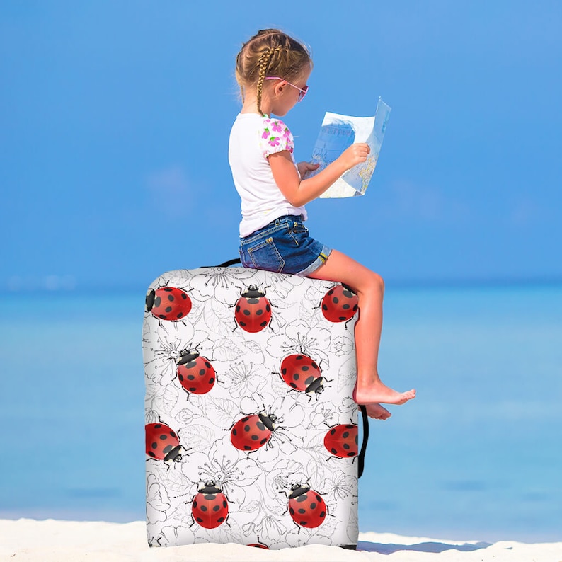 May include: A white suitcase cover with a black and white floral pattern and red ladybugs. A young girl is sitting on the suitcase, looking at a map.