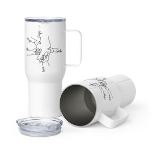 May include: White travel mug with a handle and a lid. The mug features a black line drawing of hands holding each other, with names like "Hugo" and "Lucie" written next to them. The mug is designed for hot or cold beverages.