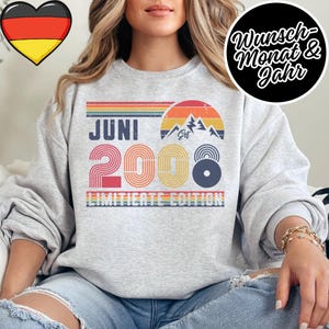 K&ouml;nnte beinhalten: Hellgraues Sweatshirt mit Retro-Design. Das Design umfasst den Text "JUNI 2008" in Rot, Gelb und Blau, eine Berg-Grafik und die Worte "LIMITED EDITION". Ein Herz mit der deutschen Flagge befindet sich in der oberen linken Ecke.