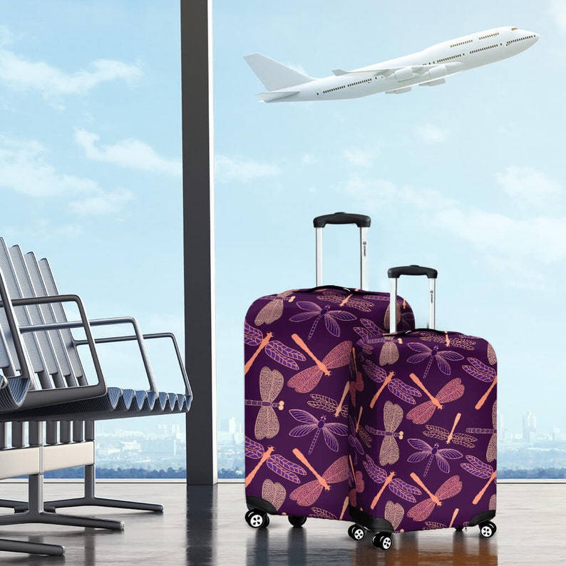 May include: Two purple luggage bags with a dragonfly pattern. The larger bag is in the foreground and the smaller bag is behind it. The bags are in an airport terminal with a plane flying overhead.