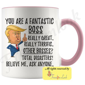 May include: White ceramic coffee mug with a pink rim and handle. The mug features a cartoon image of Donald Trump with the text "You are a fantastic boss. Really great. Really terrific. Other bosses? Total disasters! Believe me. Ask anyone."