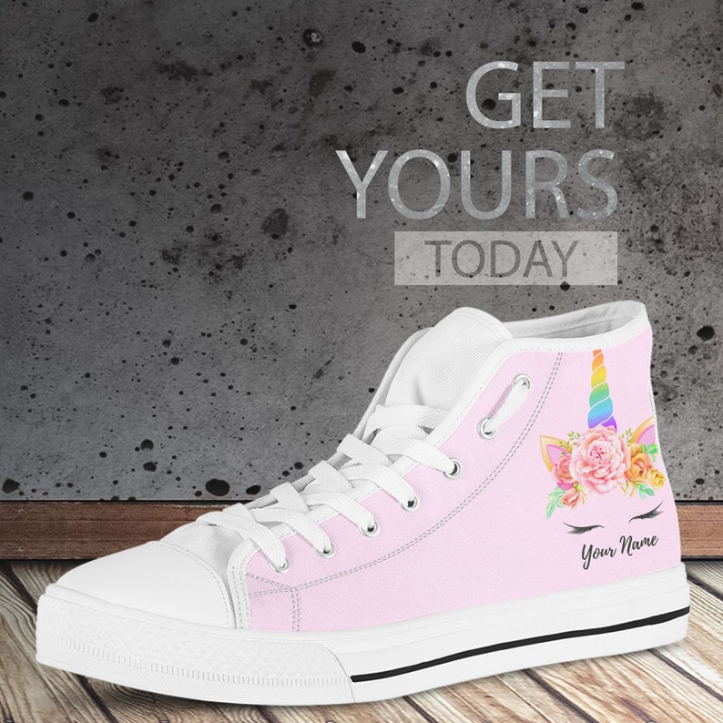 May include: Pink high-top canvas shoes with a unicorn design featuring a rainbow horn, flowers, and eyelashes. The shoes have white laces and a black trim around the sole. The text "Your Name" is printed on the side of the shoe.