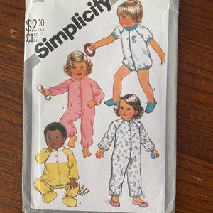 May include: Simplicity sewing pattern number 5593 for toddler pajamas. The pattern includes four different styles of pajamas: a white one with blue trim, a pink one with white trim, a yellow one with white trim, and a white one with a floral print.