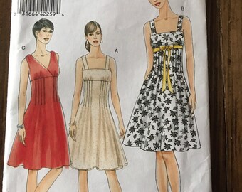 May include: Vogue sewing pattern number V8488 for a dress. The pattern includes three different styles: a red dress with a V-neck, a cream dress with a square neckline, and a black and white floral dress with a square neckline and a yellow ribbon.