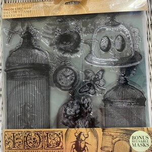 May include: Clear plastic stamp set featuring vintage-style designs. Includes birdcages, a pocket watch, a butterfly, and a bird's nest. The packaging reads "Iron Orchid Designs" and "Bonus Reusable Masks."