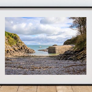 Op de afbeelding: Een foto van een rotsachtige baai met een klein zeilbootje in de verte. De baai wordt omringd door rotsachtige kliffen en het water is kalm en blauw. De lucht is bewolkt en de zon schijnt.