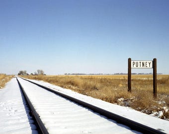 Photograph of Putney in South Dakota, USA - town sign next to rail tracks heading into the distance towards a few houses in a snowy scene