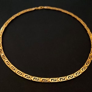 May include: A gold chain necklace with a Greek key pattern.