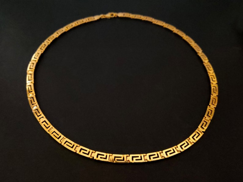 May include: A gold chain necklace with a Greek key pattern.