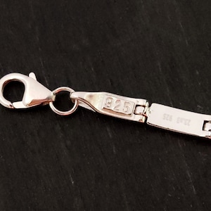 Puede incluir: Primer plano de una cadena de plata con un cierre de langosta. La cadena est&aacute; estampada con 925, lo que indica que est&aacute; hecha de plata de ley.