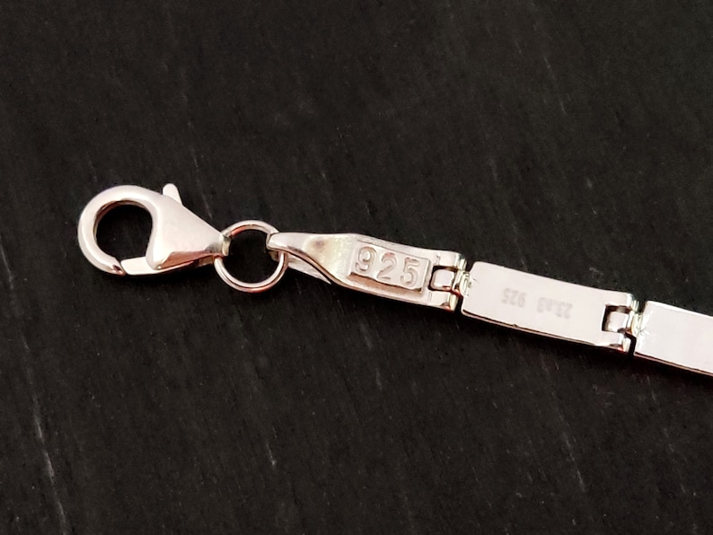 Puede incluir: Primer plano de una cadena de plata con un cierre de langosta. La cadena est&aacute; estampada con 925, lo que indica que est&aacute; hecha de plata de ley.