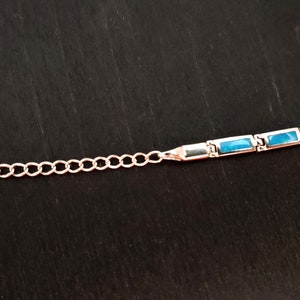 Puede incluir: Un brazalete de plata con una cadena y piedras rectangulares azules.
