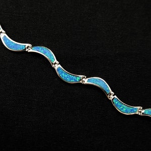 May include: A silver bracelet with a wave-like design. Each wave is inlaid with a vibrant blue opal, creating a shimmering effect. The bracelet is composed of several connected segments.