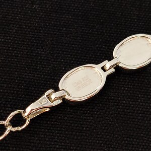 May include: A silver bracelet with oval links. The bracelet has a lobster clasp closure and a chain. The links are connected by small bars. The bracelet is marked "925" and "Greece".