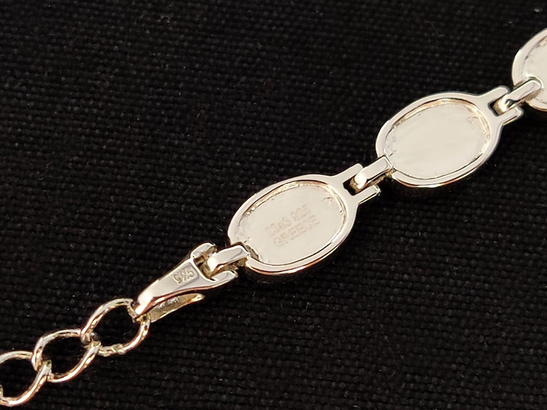 May include: A silver bracelet with oval links. The bracelet has a lobster clasp closure and a chain. The links are connected by small bars. The bracelet is marked "925" and "Greece".
