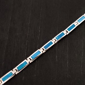 Puede incluir: Un brazalete de plata con piedras rectangulares de &oacute;palo azul. El brazalete est&aacute; hecho de piezas de metal unidas.