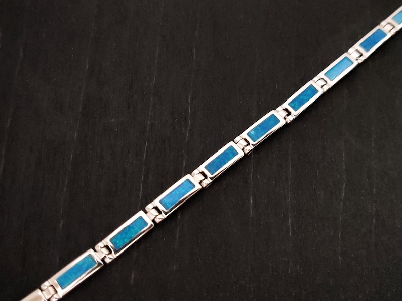 Puede incluir: Un brazalete de plata con piedras rectangulares de &oacute;palo azul. El brazalete est&aacute; hecho de piezas de metal unidas.