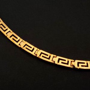 May include: A gold chain necklace with a Greek key pattern.