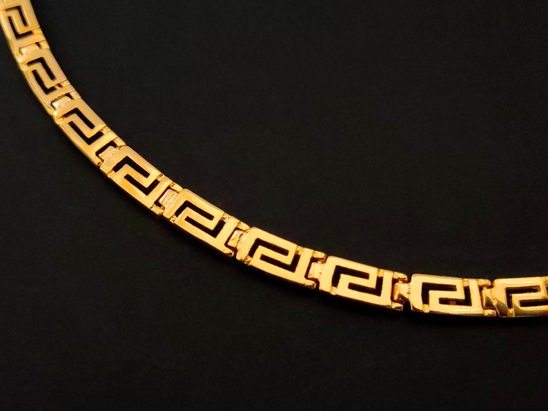 May include: A gold chain necklace with a Greek key pattern.