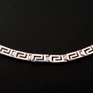 May include: A silver chain necklace with a Greek key pattern.