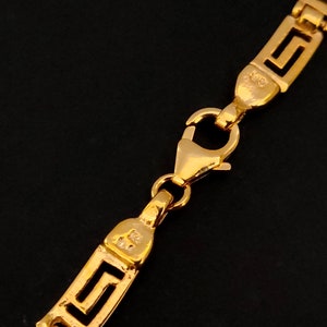 May include: Gold chain necklace with a Greek key pattern and a lobster clasp closure.
