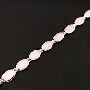 Puede incluir: Un brazalete de plata con piedras de &oacute;palo blanco de forma ovalada. El brazalete est&aacute; hecho de una cadena delicada y presenta un dise&ntilde;o simple.