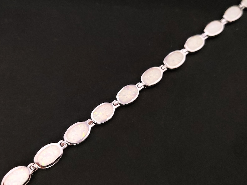 Puede incluir: Un brazalete de plata con piedras de &oacute;palo blanco de forma ovalada. El brazalete est&aacute; hecho de una cadena delicada y presenta un dise&ntilde;o simple.