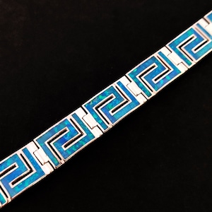 May include: A silver bracelet with a blue opal inlay in a Greek key pattern.