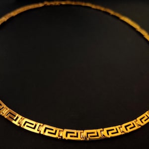 May include: A gold-colored necklace with a Greek key pattern.