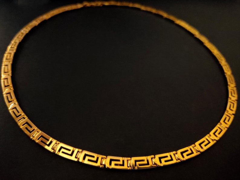 May include: A gold-colored necklace with a Greek key pattern.