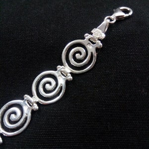 May include: A silver bracelet with a spiral design. The bracelet features three openwork spiral links connected by smaller decorative elements. The clasp is a lobster claw style. The bracelet is displayed against a black background.