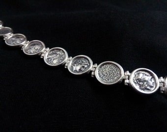 May include: Silver bracelet with round coin-shaped charms featuring embossed images of historical figures and designs.