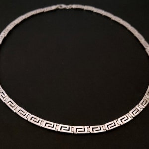 May include: A silver necklace with a Greek key pattern.