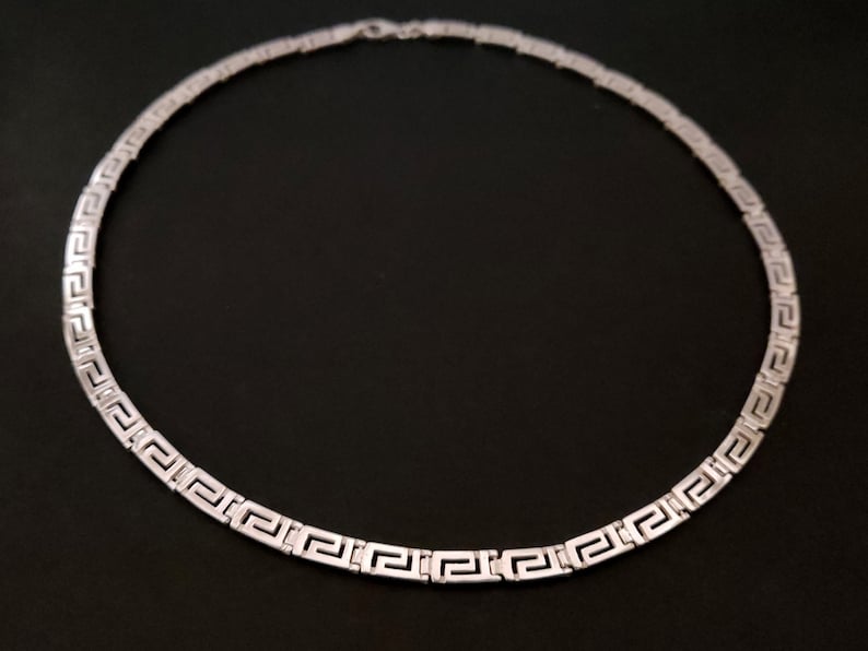 May include: A silver necklace with a Greek key pattern.