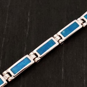 Puede incluir: Un brazalete de plata con piedras rectangulares de &oacute;palo azul. El brazalete tiene un dise&ntilde;o de cadena de eslabones.