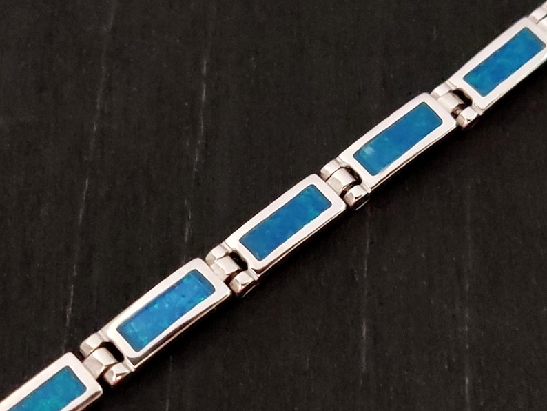 Puede incluir: Un brazalete de plata con piedras rectangulares de &oacute;palo azul. El brazalete tiene un dise&ntilde;o de cadena de eslabones.