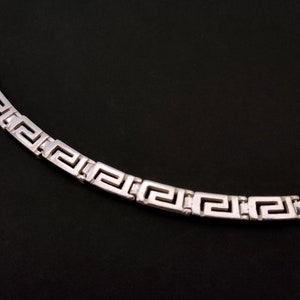 May include: A silver necklace with a Greek key pattern.