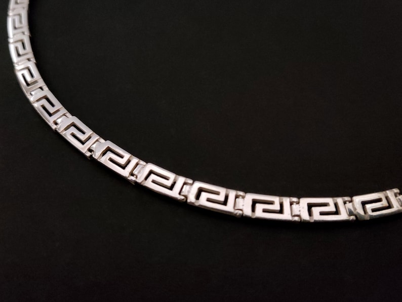 May include: A silver necklace with a Greek key pattern.