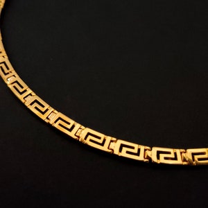 May include: A gold chain necklace with a Greek key pattern.