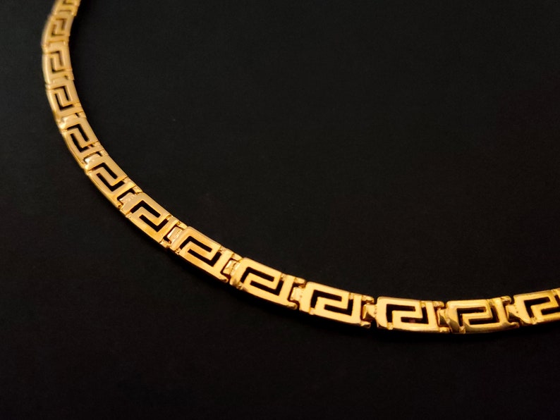 May include: A gold chain necklace with a Greek key pattern.