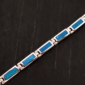 Puede incluir: Un brazalete de plata con piedras de &oacute;palo azul rectangulares. El brazalete est&aacute; hecho de piezas de metal unidas.
