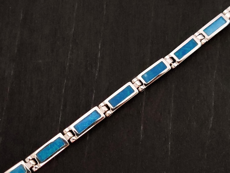 Puede incluir: Un brazalete de plata con piedras de &oacute;palo azul rectangulares. El brazalete est&aacute; hecho de piezas de metal unidas.