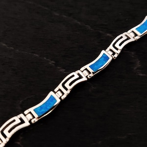 Pode incluir: Uma pulseira de prata com uma incrustação de opala azul e um design de chave grega.