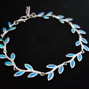 May include: A silver bracelet with a delicate design of blue opal leaves. The bracelet is made of sterling silver and features a delicate chain with a lobster clasp.