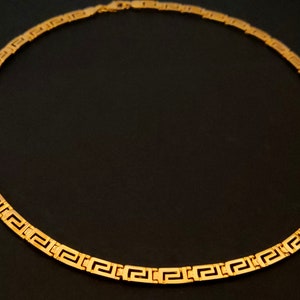 May include: A gold chain necklace with a Greek key pattern.
