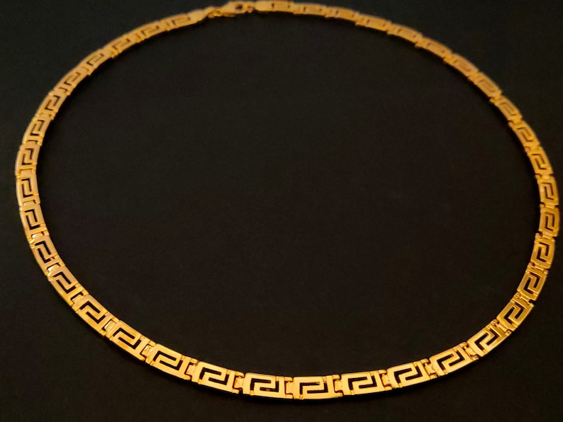 May include: A gold chain necklace with a Greek key pattern.
